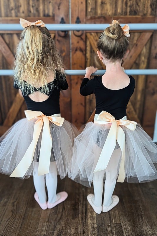Two young dancers at the barre with satin bows and tulle skirts